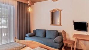Camera da letto con un letto in legno, un divano blu, una sedia di legno, una televisione e una finestra con tende.