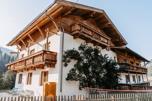 Ein traditionelles Holzhäuschen mit geneigtem Dach, Holzbalkonen und einem großen Baum davor.