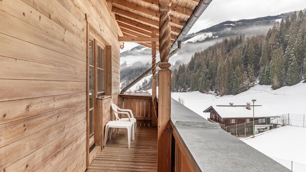 Una baita di legno con un balcone che si affaccia su un paesaggio montano innevato.
