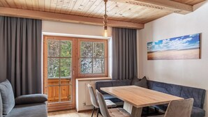 Una stanza con soffitto in legno, una grande finestra con tende, un tavolo da pranzo con sedie, una panca e un quadro appeso al muro.