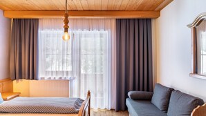 A room with a bed, a sofa, a wooden ceiling, and a window with curtains.