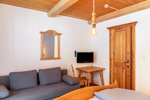 A room with a wooden ceiling, a wooden door, a gray sofa, a small wooden table, and a television mounted on the wall. - Holiday Apartment "Schwüwong - Apartment 13" with Mountain View, Shared Terrace and Wi-Fi (Kelchsau)