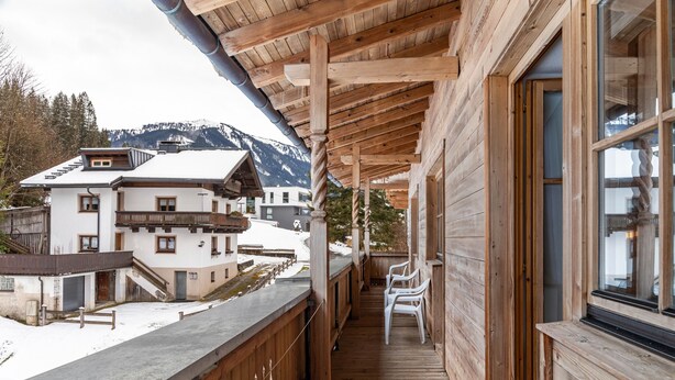 A wooden balcony with a view of snow-covered mountains and a building with a sloped roof.