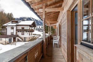 A wooden balcony with a view of snow-covered mountains and a building with a sloped roof.