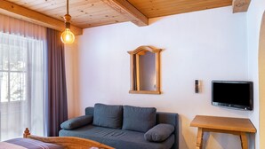 A room with a wooden ceiling, a sofa, a bedside table, a TV, and a window with curtains.