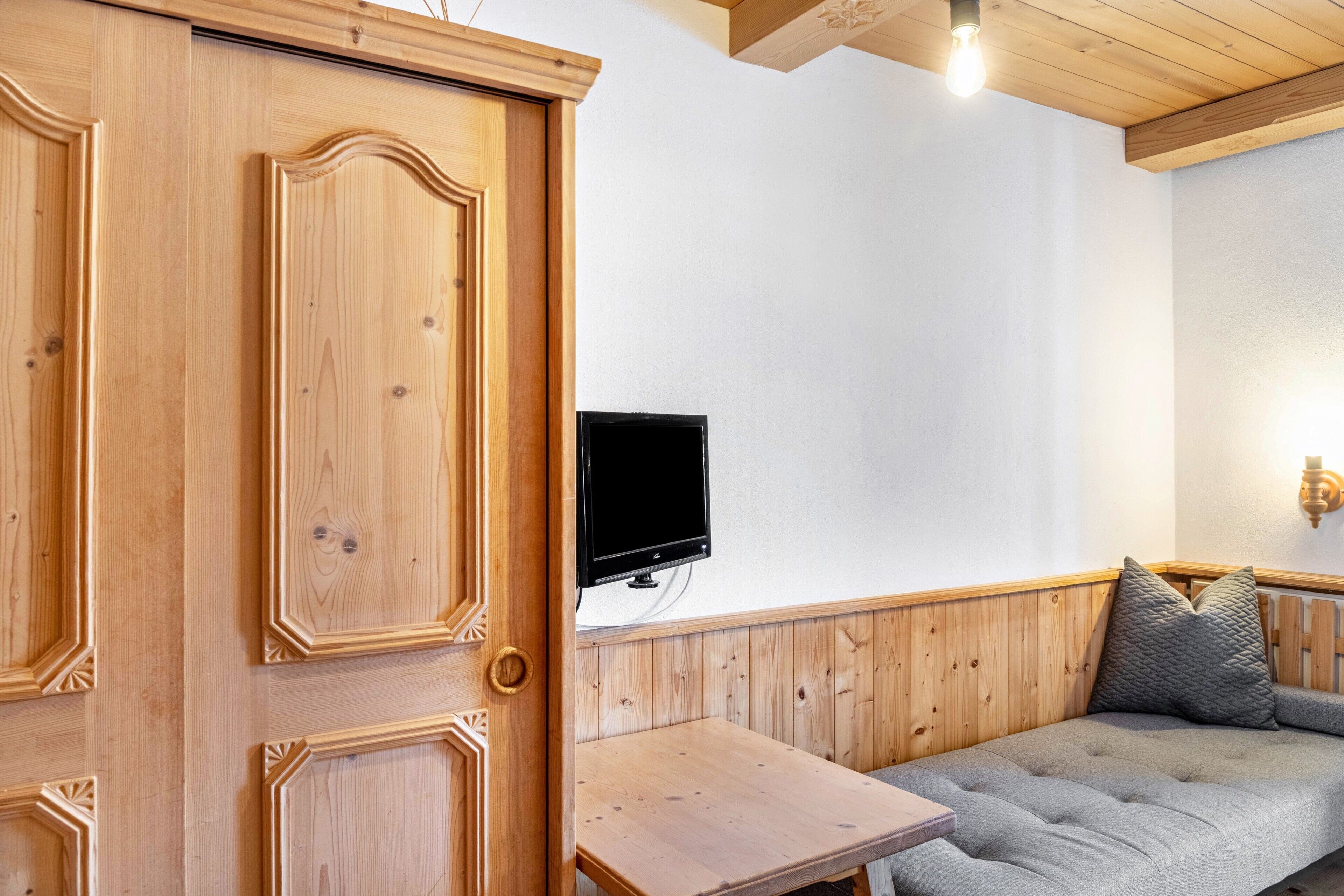 A wooden door, a flat-screen TV mounted on the wall, and a wooden bench.