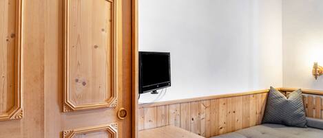 A wooden door, a flat-screen TV mounted on the wall, and a wooden bench.