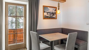 A dining area with a wooden table and cushioned bench, a window with a view of trees, and a framed picture on the wall.