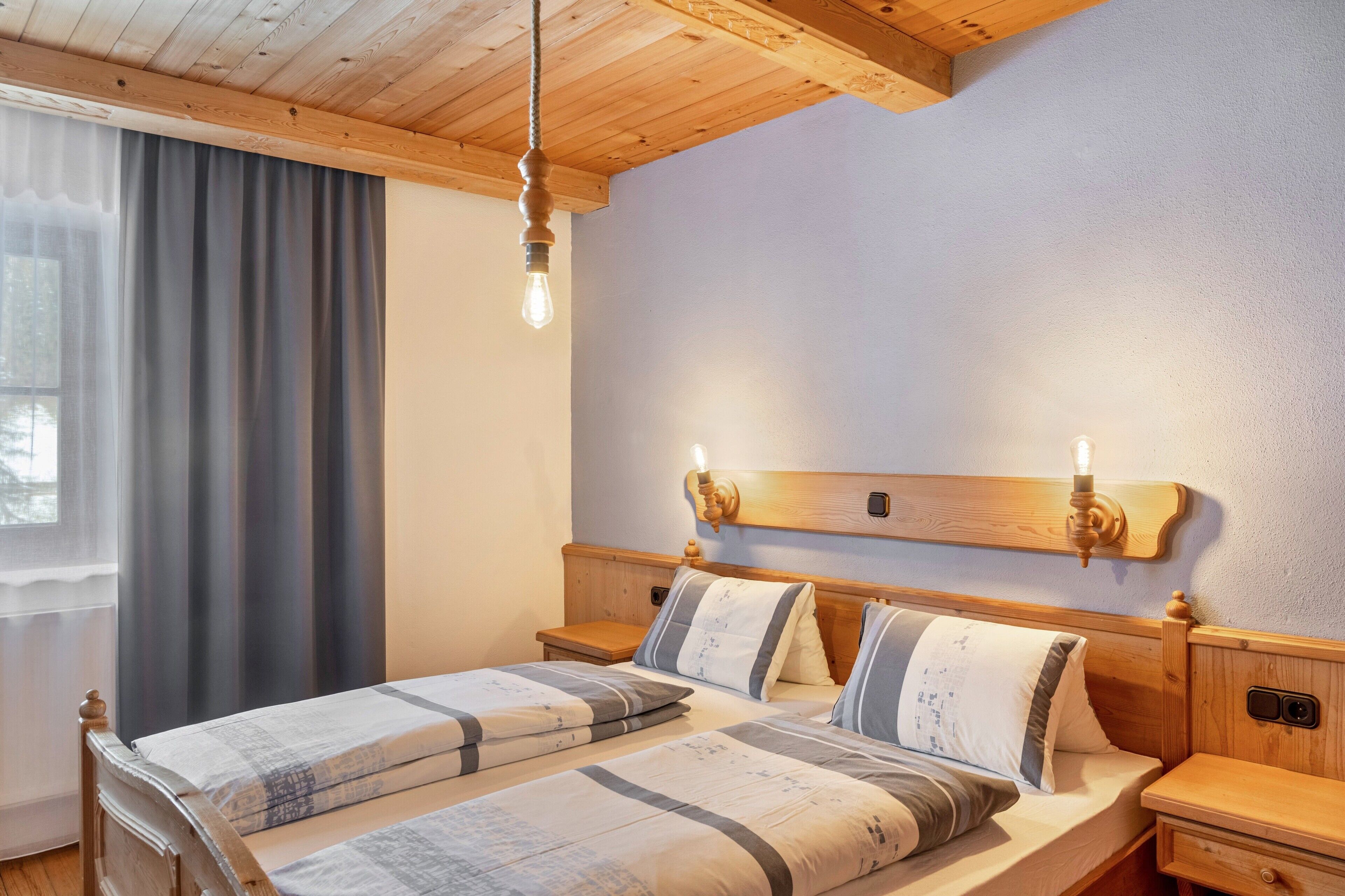A double bed with a wooden headboard, bedside tables, and a hanging light fixture.