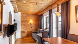 A cozy room with a wooden ceiling, a sofa, a dining table, and a TV mounted on the wall.