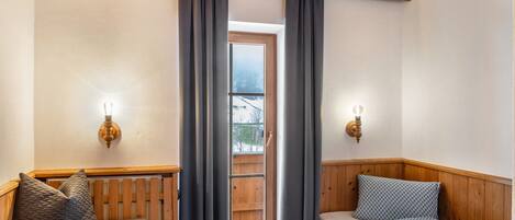 A cozy room with a wooden ceiling, a window with curtains, a radiator, and a bed with patterned bedding.