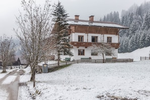 A two-story building with a wooden balcony, a metal roof, and a snow-covered landscape.