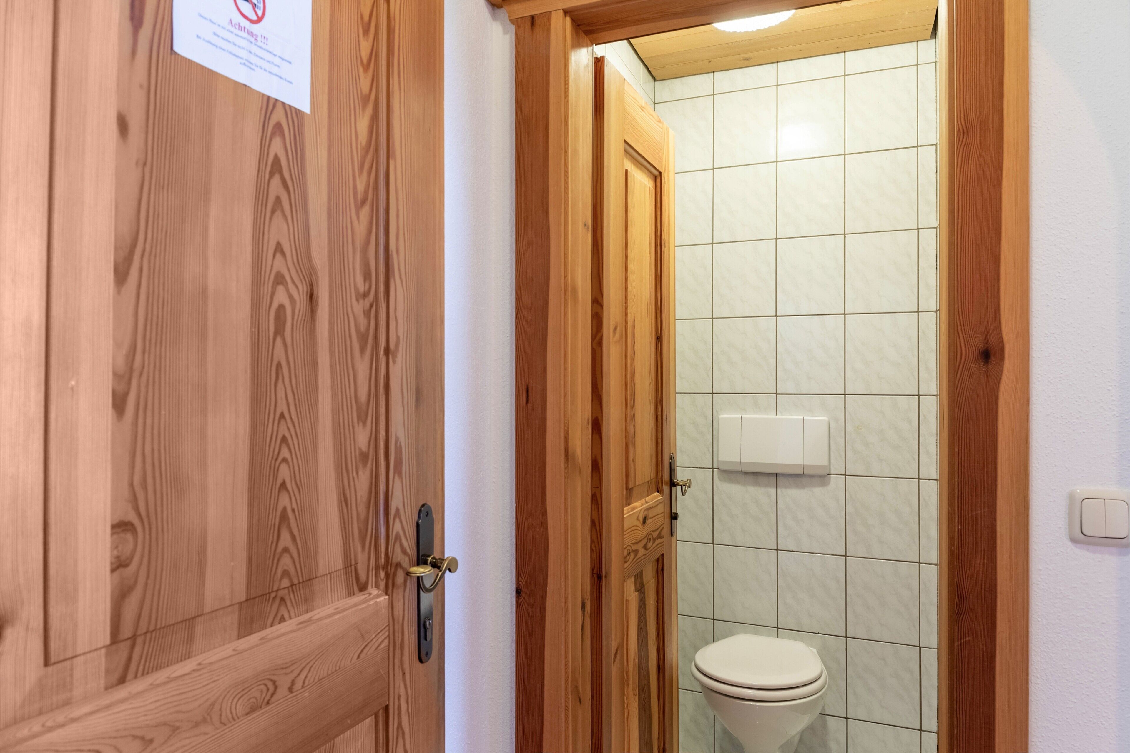 A wooden door with a sign, a tiled wall, and a toilet.