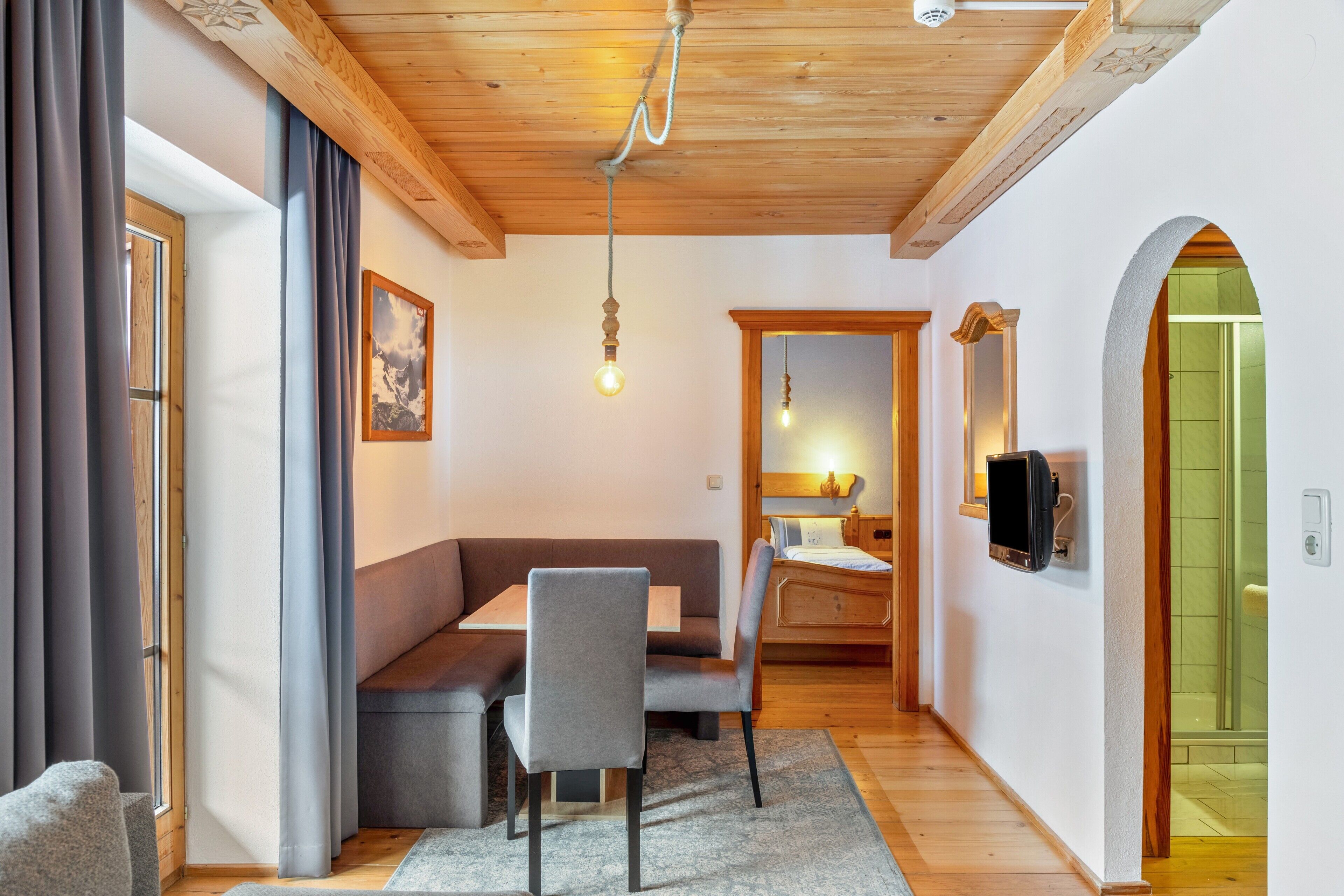 Een modern interieur met een houten plafond, een zithoek met een tafel en stoelen, een bed en een douchegedeelte.