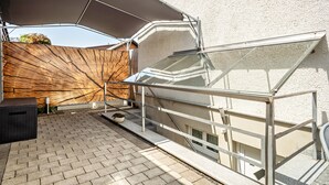 Une terrasse sur le toit, dotée d’une structure vitrée, d’une rambarde en métal et d’un grand parasol offrant de l’ombre.