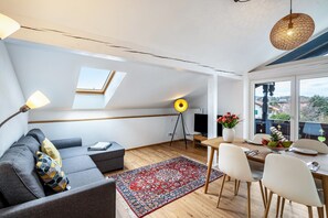 Una sala de estar moderna con un sofá, una mesa de comedor y un televisor. Hay un tragaluz y un ventanal grande.