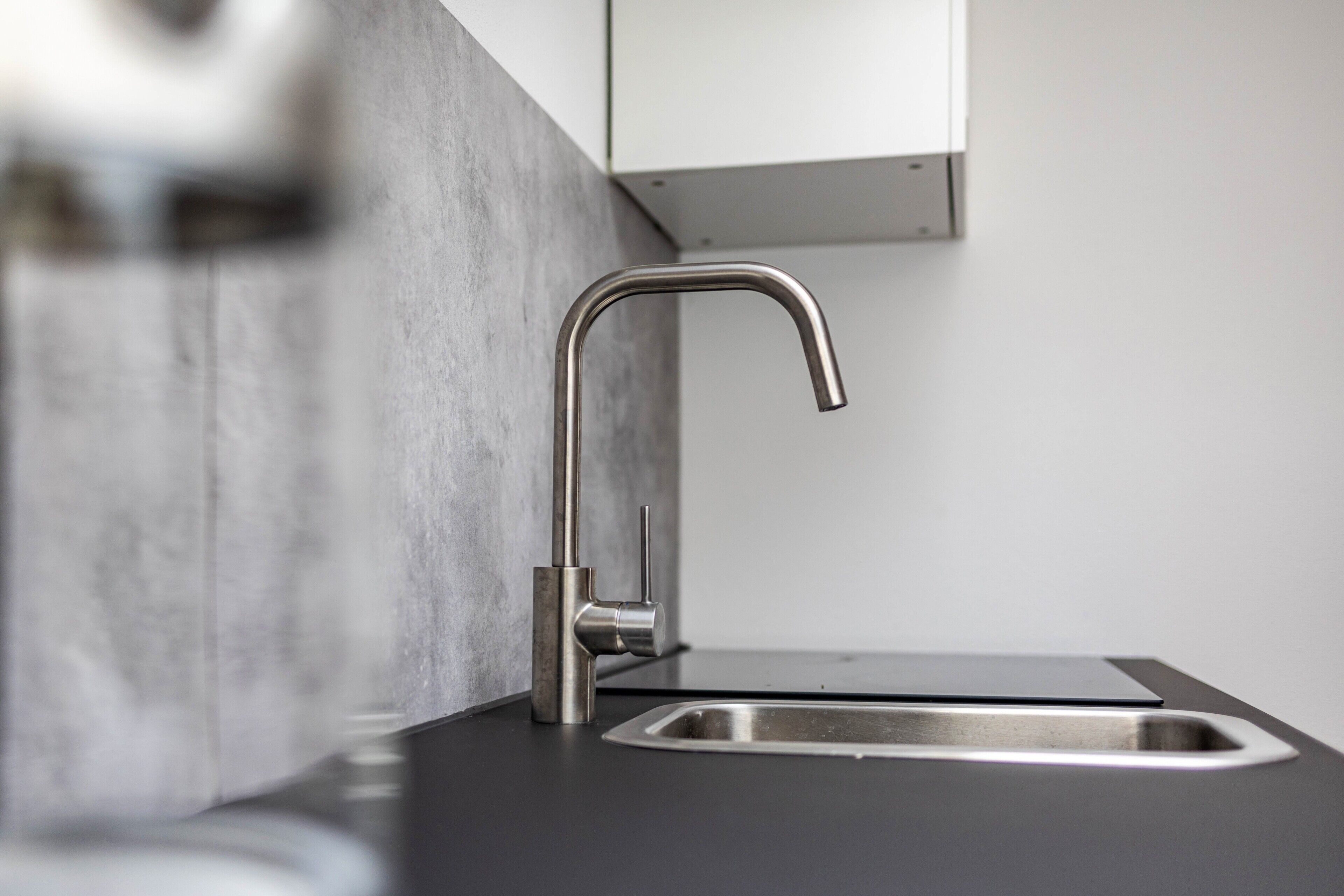 Een moderne keuken met een roestvrijstalen kraan, een zwart aanrecht en een grijze achterwand.