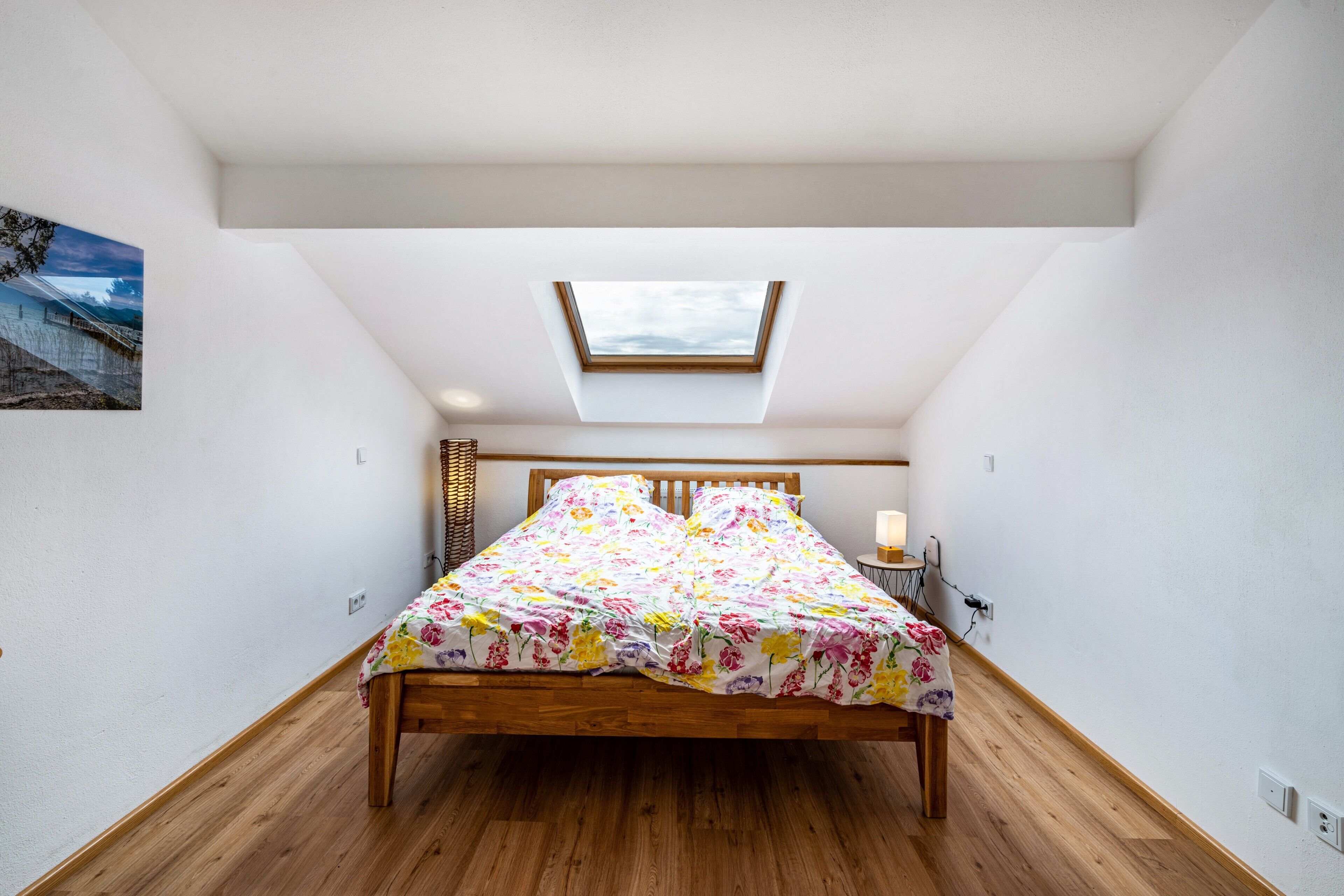 Ein Schlafzimmer mit Dachfenster, einem hölzernen Bett und einem Nachttisch mit Lampe.