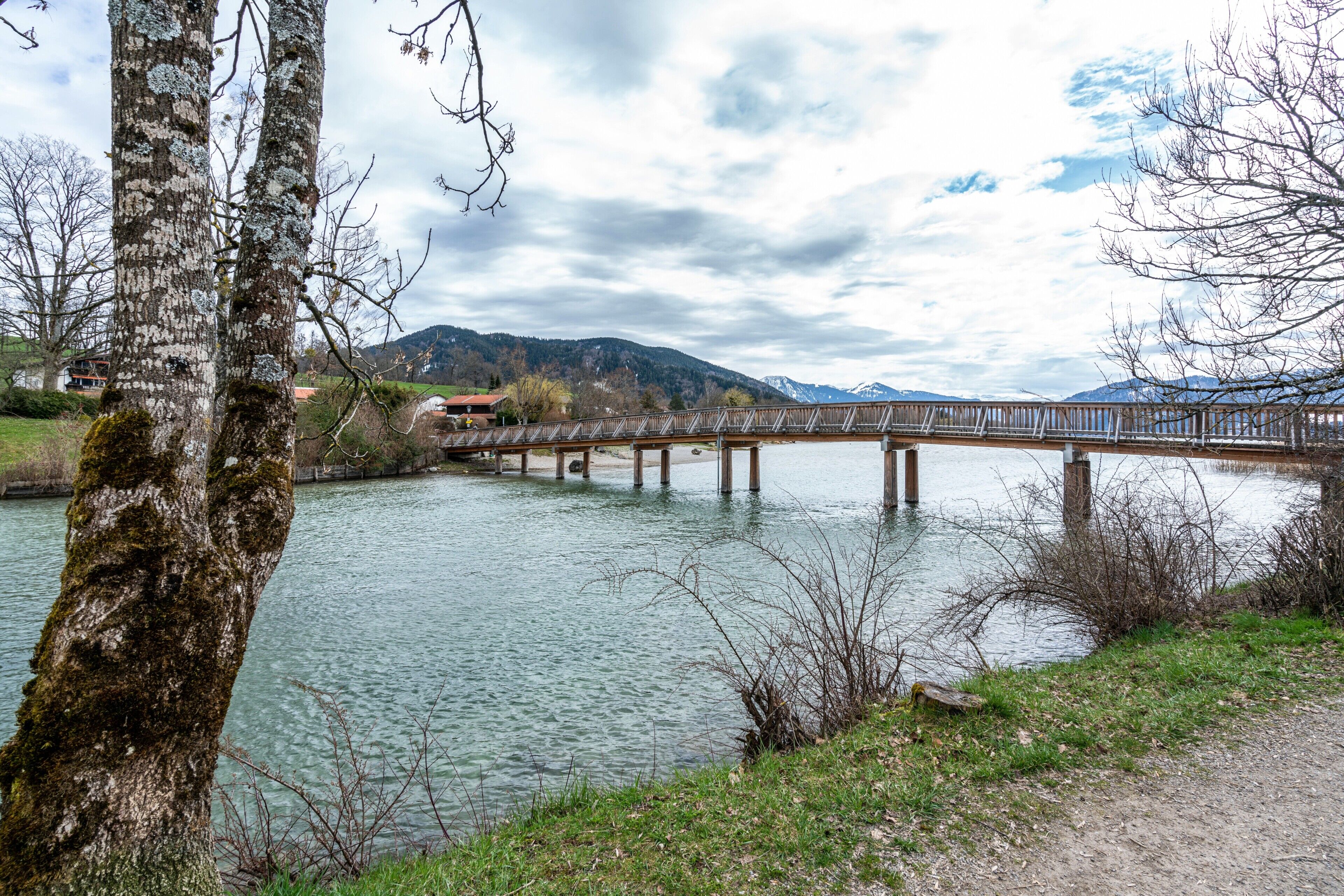 Un pont de fusta sobre un riu tranquil amb muntanyes al fons.