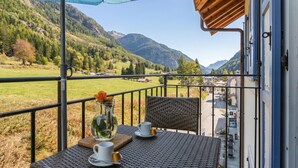 A balcony with a table, chairs, and a view of a mountainous landscape.
