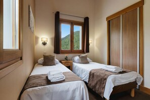 A hotel room with two beds, a window with a view of a forest, and a wooden wardrobe.