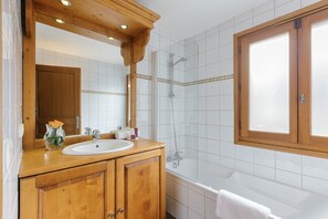 A bathroom with a wooden vanity, a sink, a mirror, and a shower area.