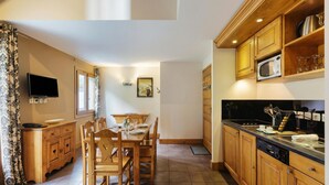 A kitchen with wooden cabinets, a dining table with chairs, a television, and a microwave. - V Buet 53: Beside Ski Lift; Pool, Sauna & Gym, Vallorcine (Argentiere), France (Vallorcine (Argentiere))