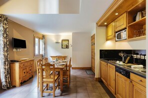 A kitchen with wooden cabinets, a dining table with chairs, a television, and a microwave.