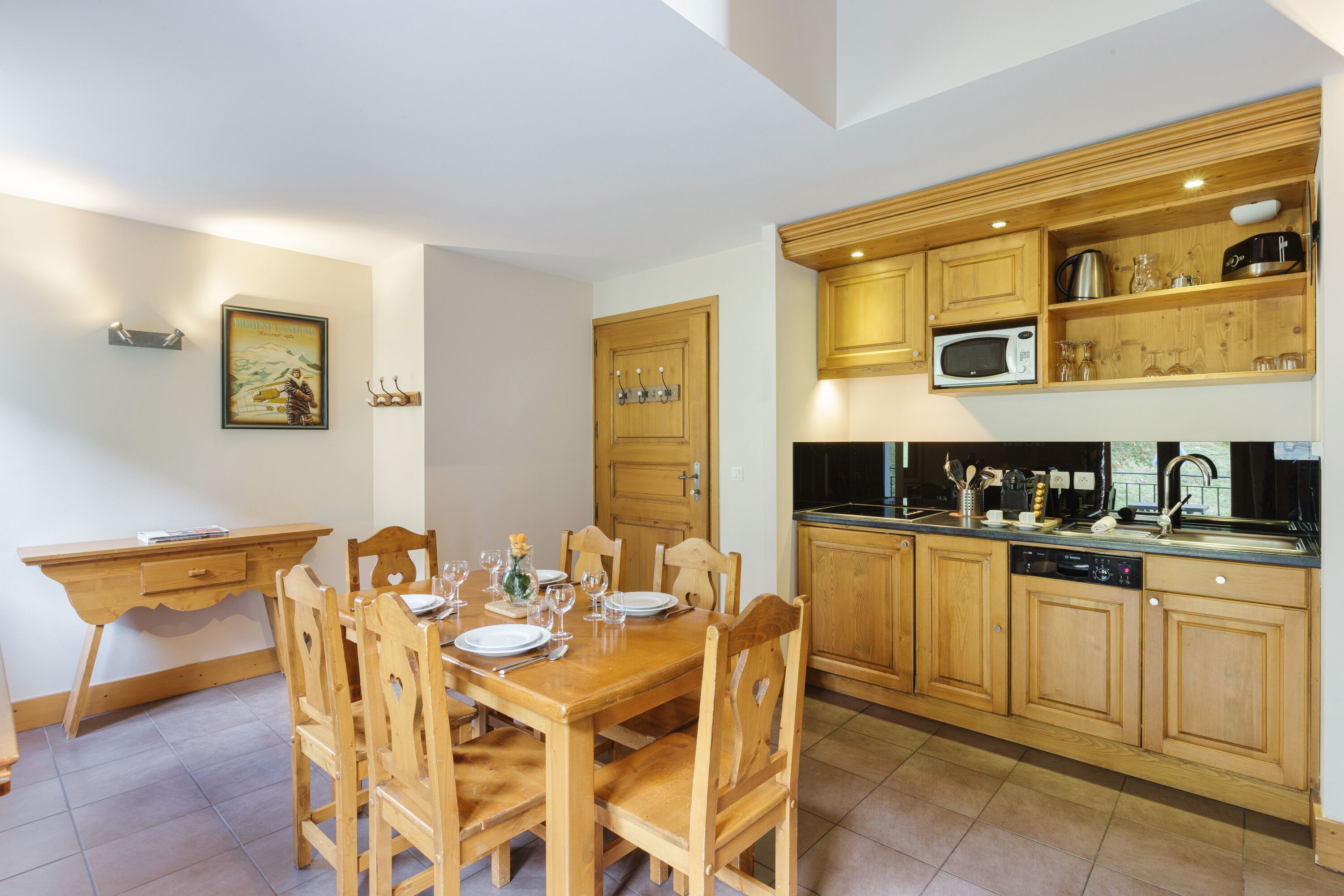 Ein Essbereich mit Holztisch und -stühlen, eine Küche mit Holzschränken und Geräten sowie ein gerahmtes Bild an der Wand.