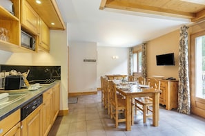 A modern kitchen with wooden cabinets, a dining area with a table and chairs, a built-in oven, and a television mounted on the wall.