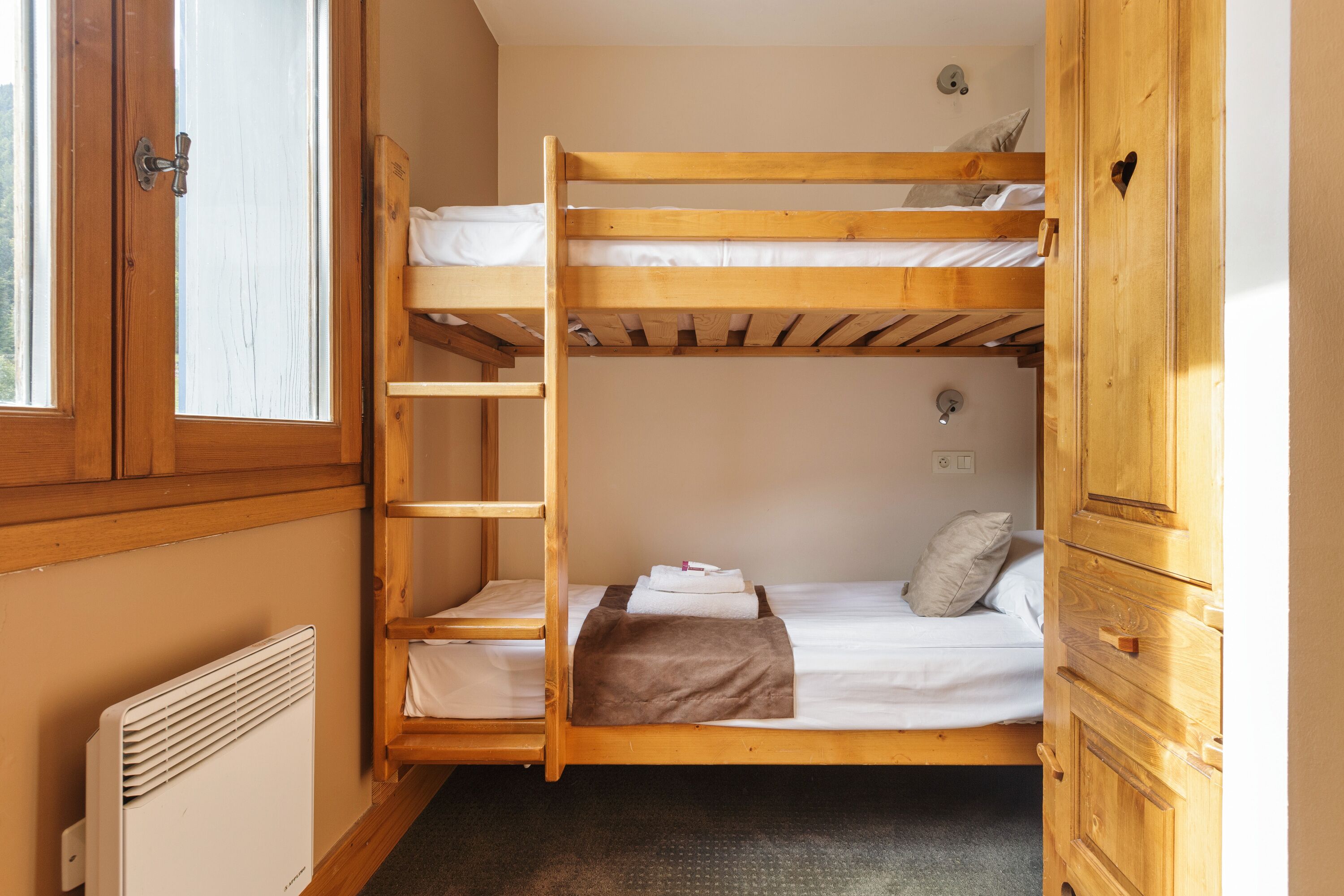 Une chambre avec un lit superposé, une échelle en bois, un radiateur et une armoire.