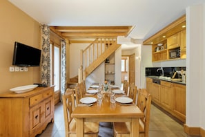 Un coin repas avec une table en bois dressée pour six personnes, des meubles de rangement en bois, un téléviseur et un escalier menant à une autre pièce.