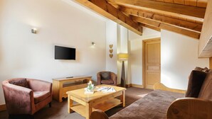 A cozy living room with a wooden ceiling, a flat-screen TV mounted on the wall, a wooden coffee table, and two leather armchairs. - V Buet 52: Beside Ski Lift; Pool, Sauna & Gym, Vallorcine (Argentiere), France (Vallorcine (Argentiere))