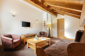 Un salon chaleureux avec un plafond en bois, un téléviseur à écran plat, une table basse en bois et deux fauteuils en cuir.