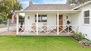 A single-story house with a covered porch, a brick chimney, and a small garden area. - Orange Blossom Cottage Near Sequoias w/EV Charger (Exeter)