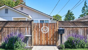 Una propiedad residencial con un portón de madera, un buzón y una casa de fachada blanca.