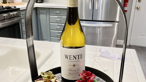 Una encimera de cocina con una botella de vino, dos cajas de regalo y un refrigerador de acero inoxidable.