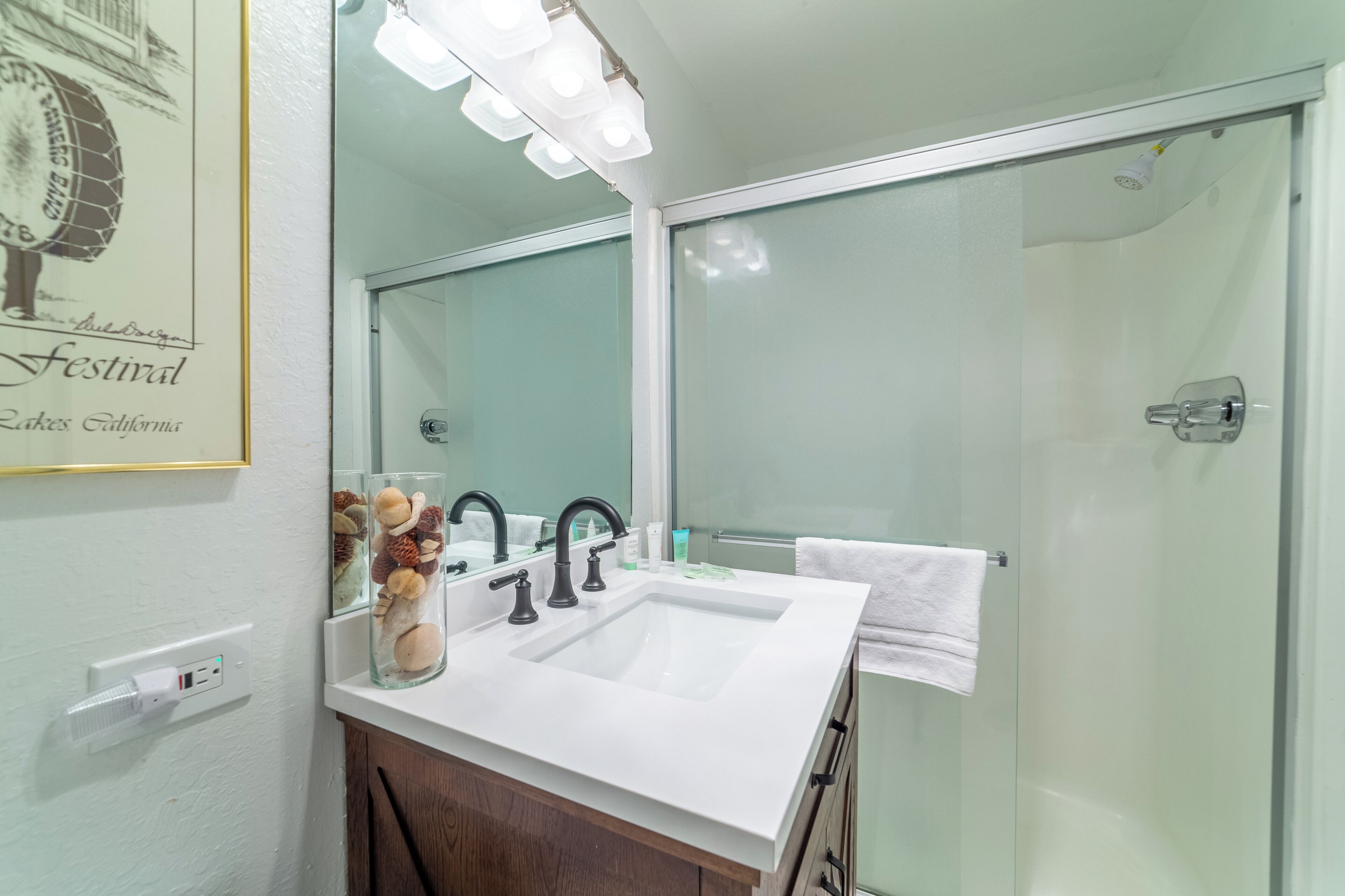 A bathroom with a white sink, two black faucets, a mirror, and a glass shower enclosure.