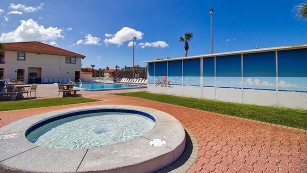 A swimming pool area with a hot tub, lounge chairs, and a building with a tiled roof.