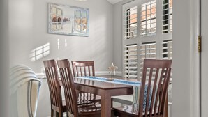A dining area with a wooden table and chairs, a decorative mirror, and a view through a window with shutters.
