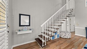 A staircase with white railings and wooden steps, a white door at the top, and a small shelf with a welcome sign.