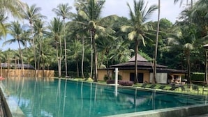 Piscina cercada por palmeiras e um pequeno edifício com telhado de palha.