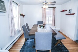 A dining room with a wooden table, grey upholstered chairs, a ceiling fan, and a blue rug. - Sunset House Near Sunday River Black Mountain (Rumford)