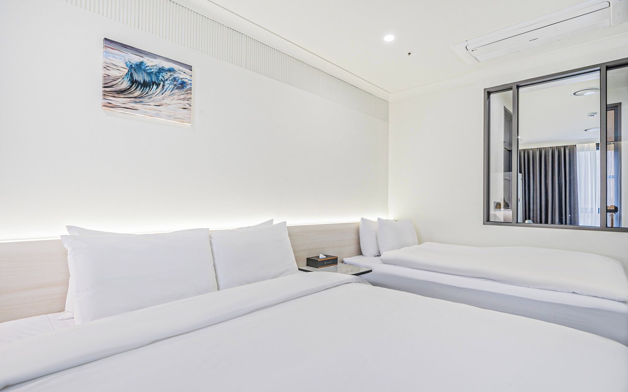 Una habitación de hotel con dos camas, una mesita de noche, un cuadro y un espejo grande.