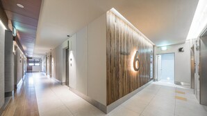 A modern hallway with a wooden accent wall, a number 6 sign, and a clean, tiled floor. - Hotel PIED Suseong (Daegu)