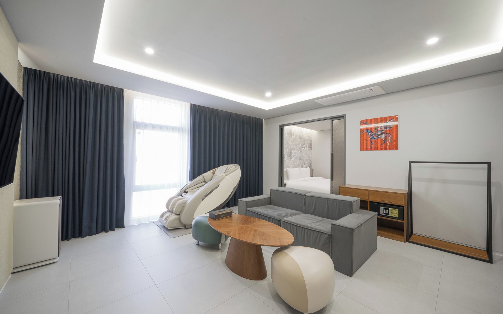 A modern hotel room with a massage chair, a sofa, a coffee table, and a bed.