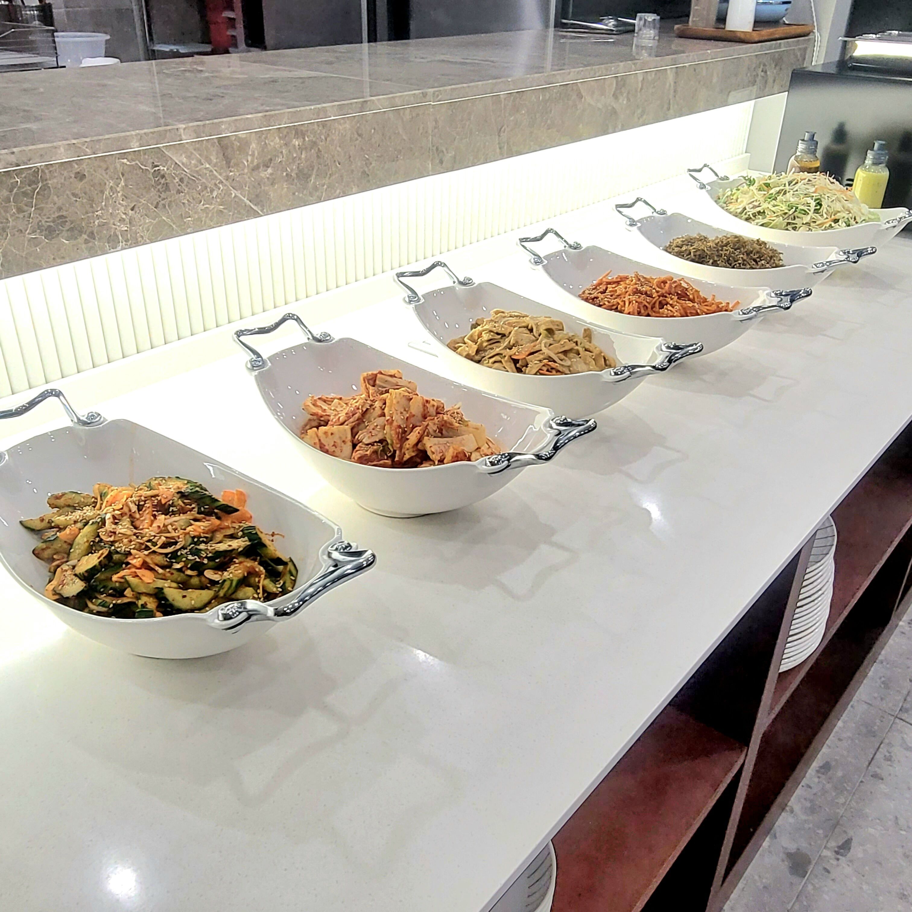 Une table de buffet avec différents plats présentés dans des bols blancs dotés d’anses.