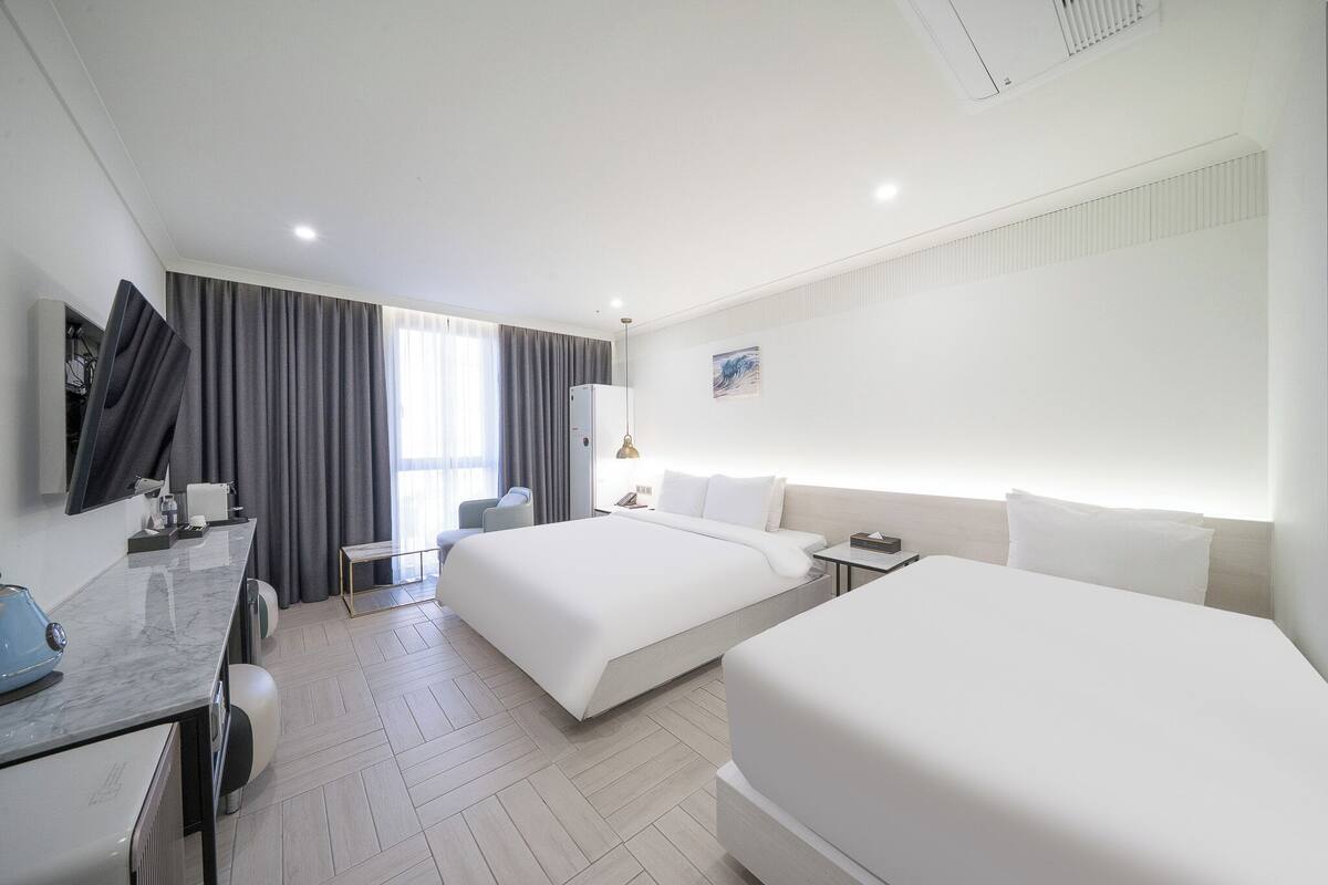 Habitación de hotel con dos camas, un escritorio, una silla, un televisor y una ventana con cortinas.