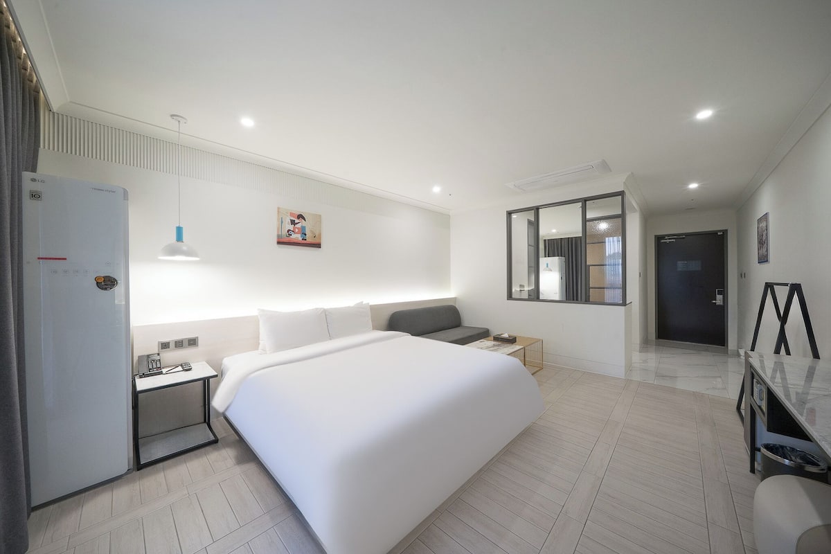 Una habitación de hotel moderna con una cama grande, mesitas de noche, un escritorio, un espejo y un armario.