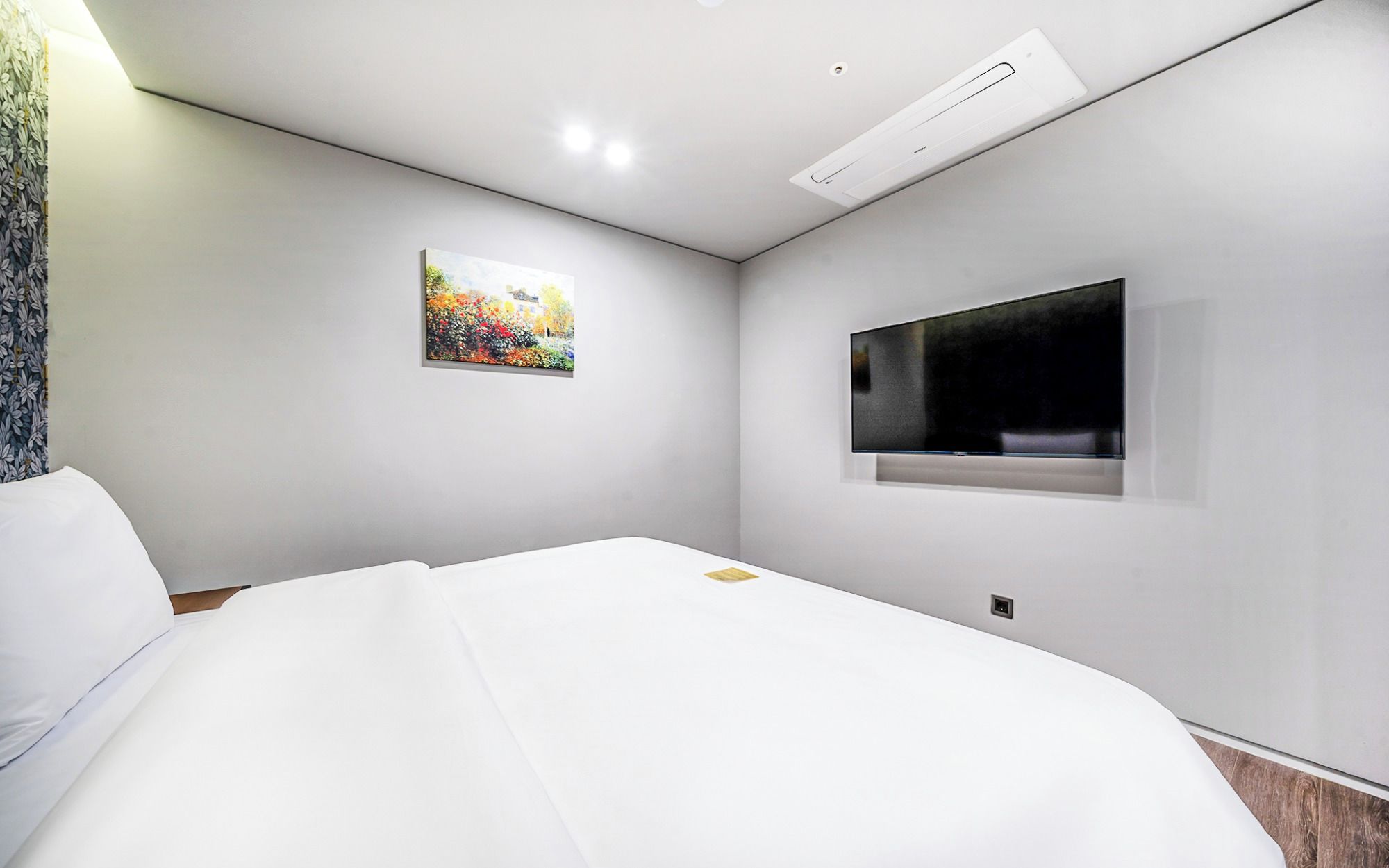 Una habitación de hotel moderna con una cama, un cuadro y un televisor fijado a la pared.